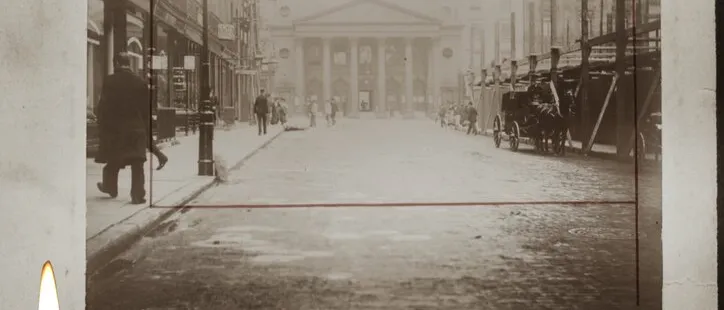 Old sepia photo of a London street and columned theatre, captioned by hand 'Le théâtre d'Heymarket', a lit candle beside