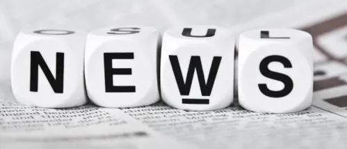 White dice with black letters spelling NEWS on a newspaper page