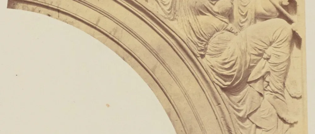 Photograph of a carved stone spandrel: a veiled, draped female figure reclining along an arch with one arm outstretched